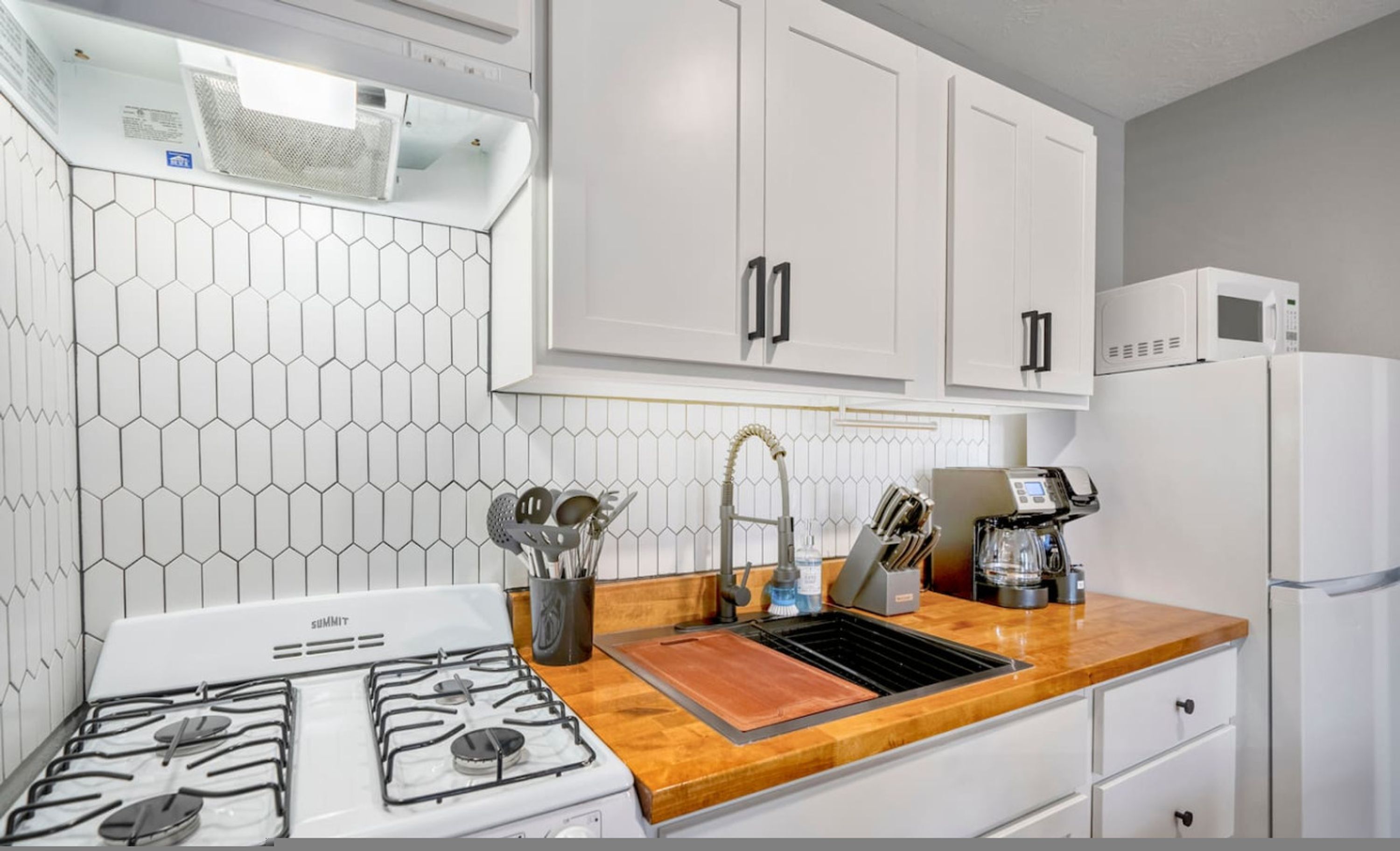 A kitchen with white cabinets, a gas stove, a sink, and a microwave.