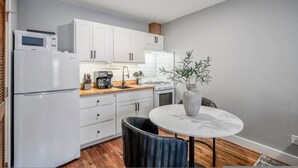 A compact kitchen with white cabinets, a microwave, a stove, and a dining area with a table and chair. - Houston Hideaway Near Dwntwn and City Attractions (Houston)