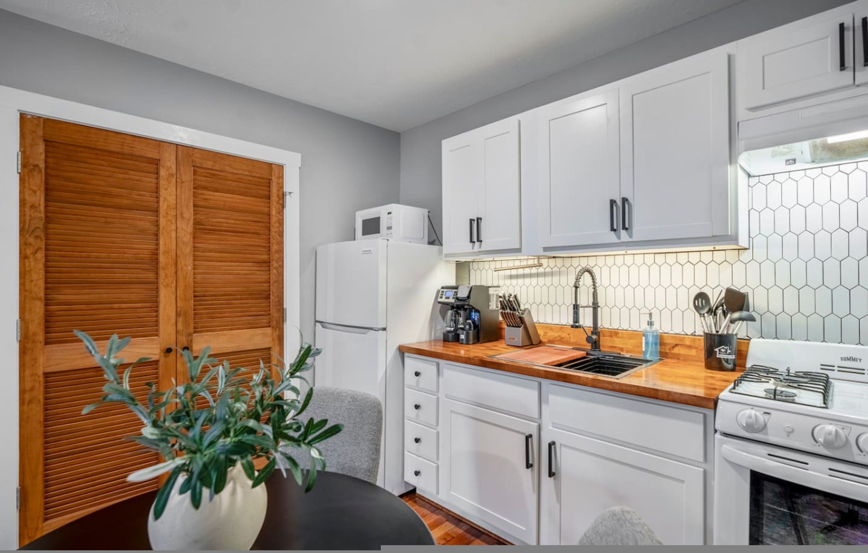 A compact kitchen with white cabinets, a microwave, a sink, and a stove.