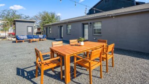 Een gebouw met een kiezelterras, een houten tafel met stoelen, een blauwe zithoek en een kleine schuur.