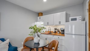 A compact kitchen with white cabinets, a white refrigerator, a microwave, and a dining area with a table and chairs. - Urban Studio Retreat Near Downtown Houston (Houston)