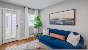 A living room with a blue sofa, a white door, a window with curtains, and a painting on the wall. - Urban Studio Retreat Near Downtown Houston (Houston)