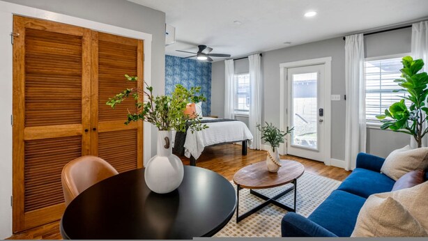 A room with a dining table, chairs, a sofa, a bed, and a large window with curtains. - Urban Studio Retreat Near Downtown Houston (Houston)