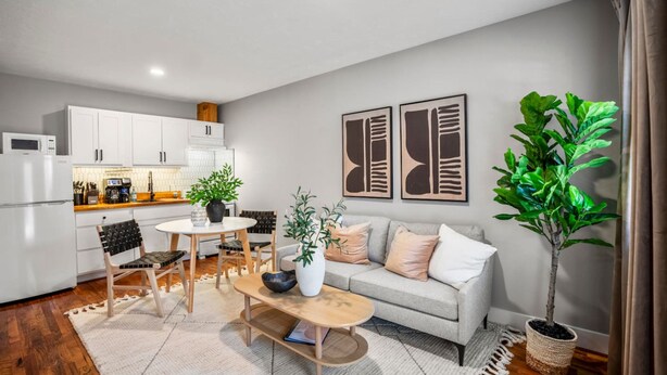 Una cocina moderna con armarios blancos, un comedor con mesa y sillas, un sofá y una planta en maceta.