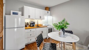 Una cocina compacta con armarios blancos, un refrigerador, una estufa y un comedor con una mesa y sillas.