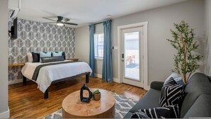 A bedroom with a bed, a round coffee table, a sofa, a ceiling fan, and a window with curtains.
