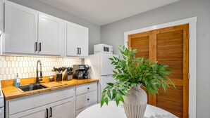 A kitchen with white cabinets, a wooden countertop, a white refrigerator, a coffee machine, and a potted plant.