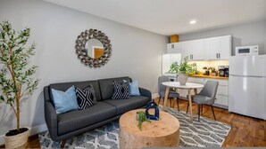 A modern living room with a grey sofa, a round coffee table, and a dining area with a white table and chairs.