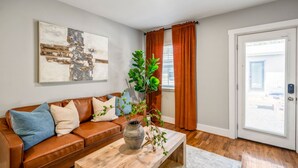 A living room with a brown leather sofa, a coffee table with a vase, a wall-mounted abstract painting, and a door with a view to the outside. - Stylish Studio Near Downtown Attractions (Houston)