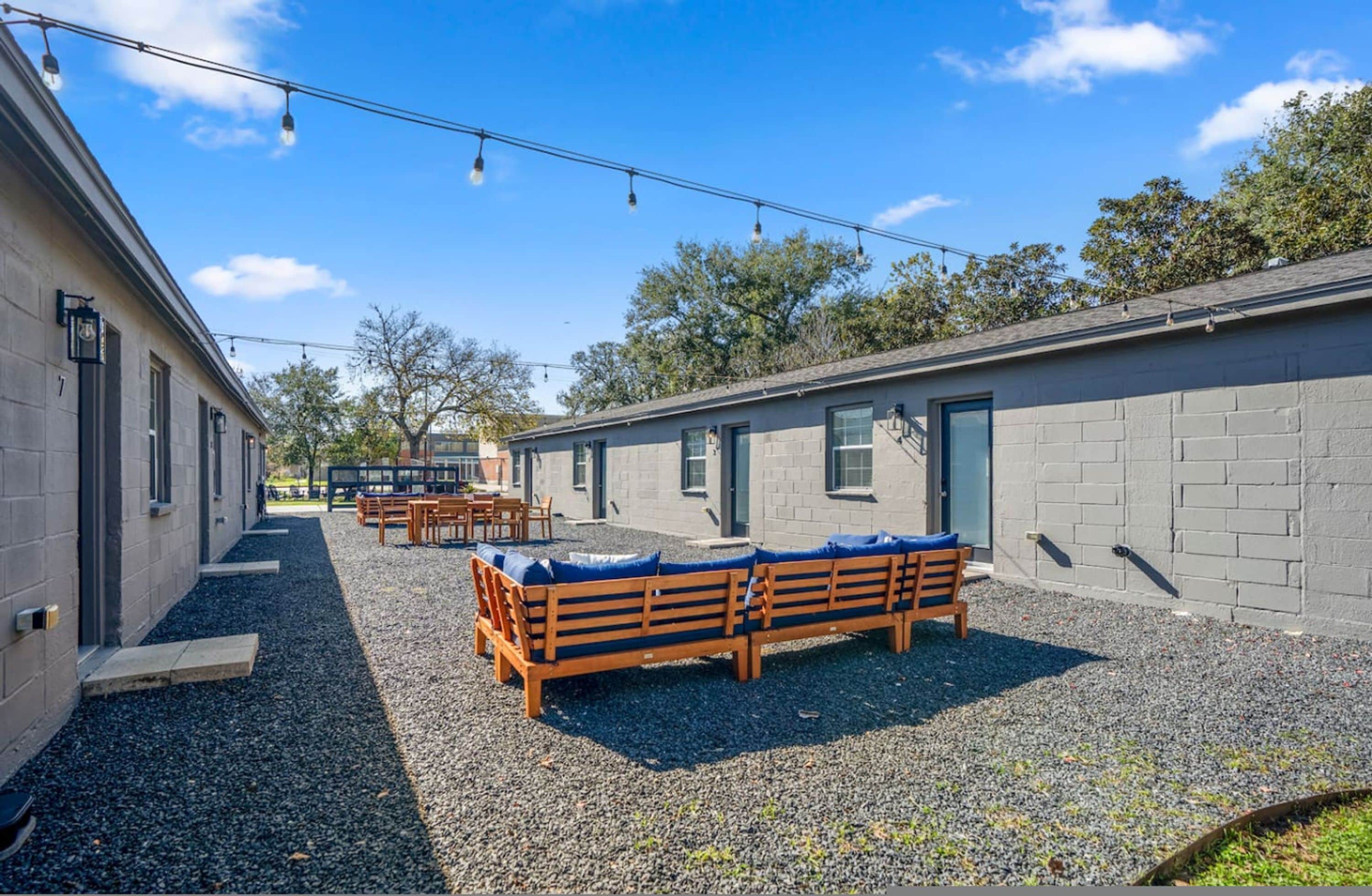 A building with a gravel courtyard, wooden benches, and string lights.
