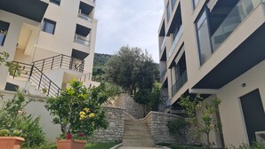 Ein modernes Apartmenthaus mit einer Steintreppe, die zu einer üppigen Grünanlage mit Bäumen und blühenden Pflanzen führt.