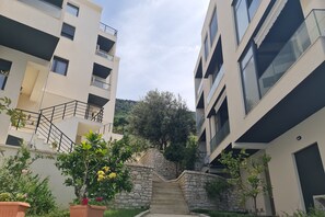 Ein modernes Apartmenthaus mit einer Steintreppe, die zu einer üppigen Grünanlage mit Bäumen und blühenden Pflanzen führt.