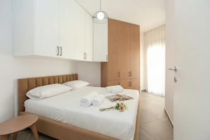 A bedroom with a bed, white and wooden cabinets, a small table, and a hanging light fixture.
