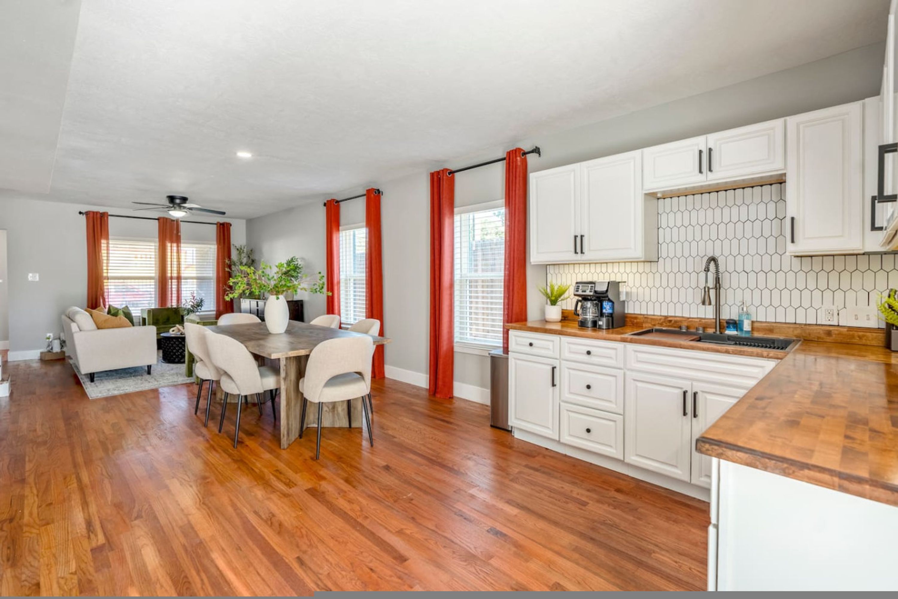 A modern kitchen with white cabinets, a wooden countertop, and a dining area with a table and chairs.