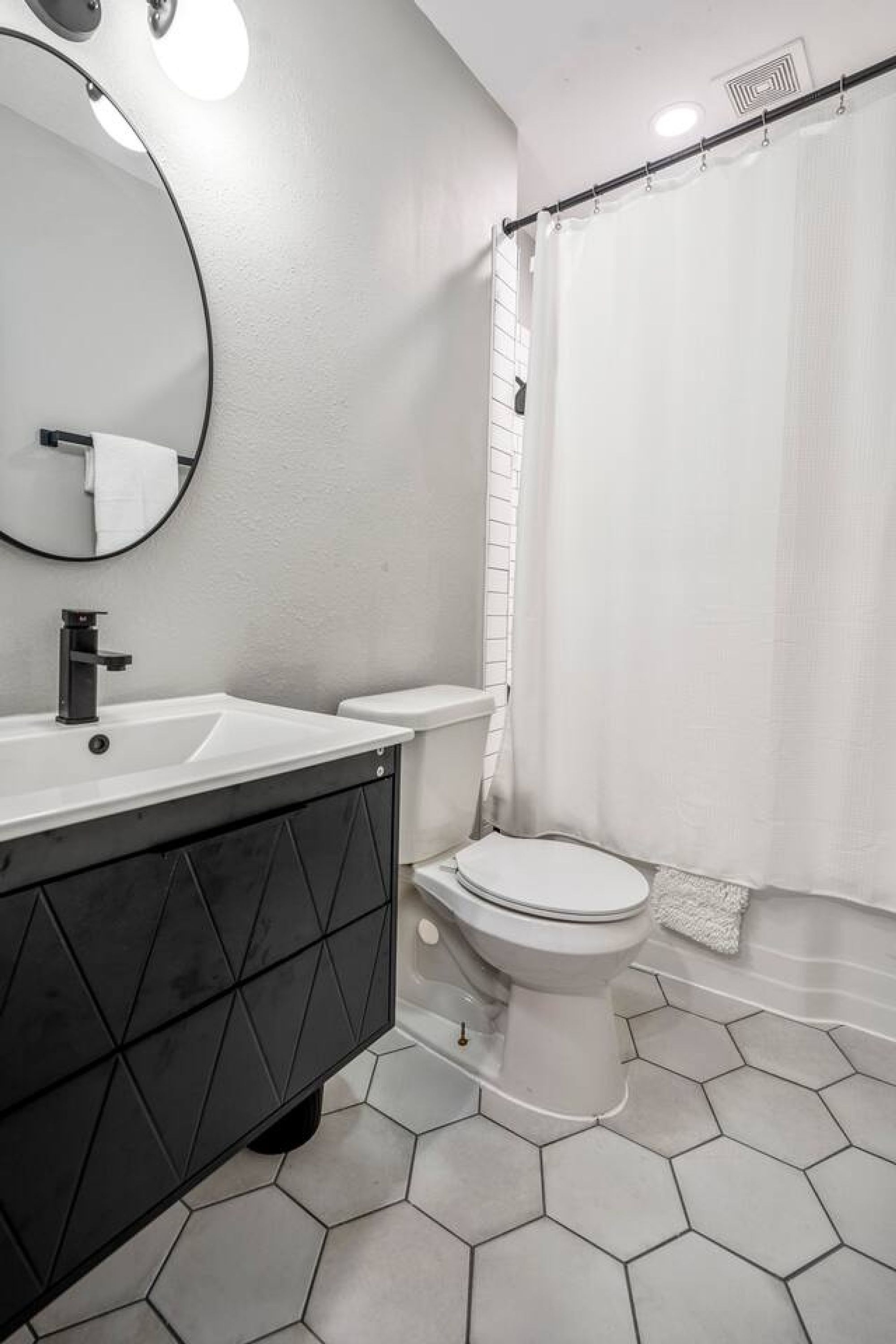 A bathroom with a white toilet, a black vanity, a round mirror, and a shower curtain.