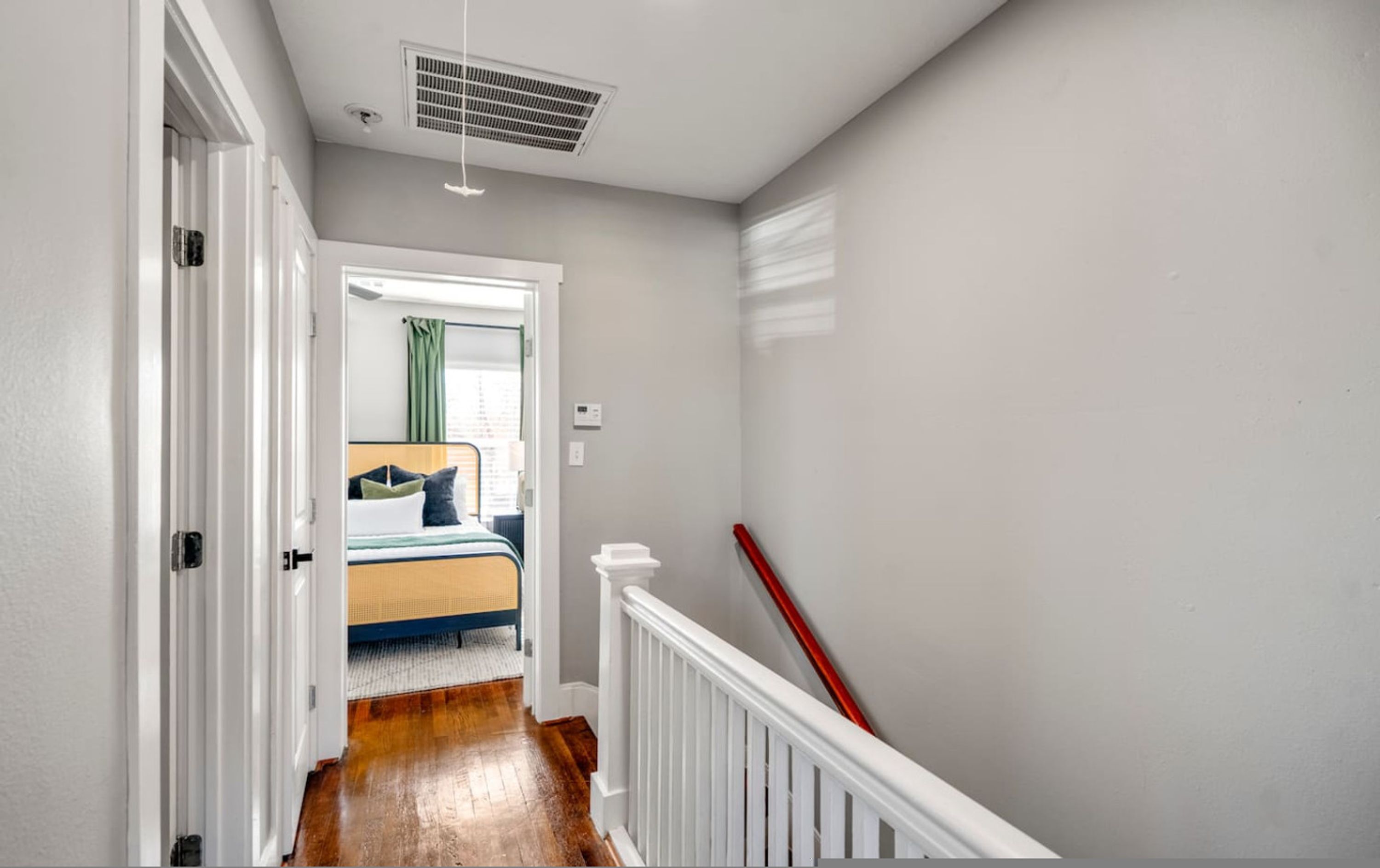 Un couloir menant à une chambre à coucher, où se trouvent un lit, une balustrade blanche et une bouche d’aération au plafond.