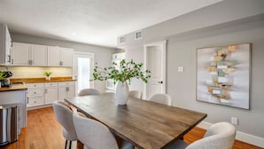 A modern kitchen with white cabinets, a wooden dining table, and a potted plant. - 2-bedroom - Equipped Kitchen - Gated Parking (Houston)