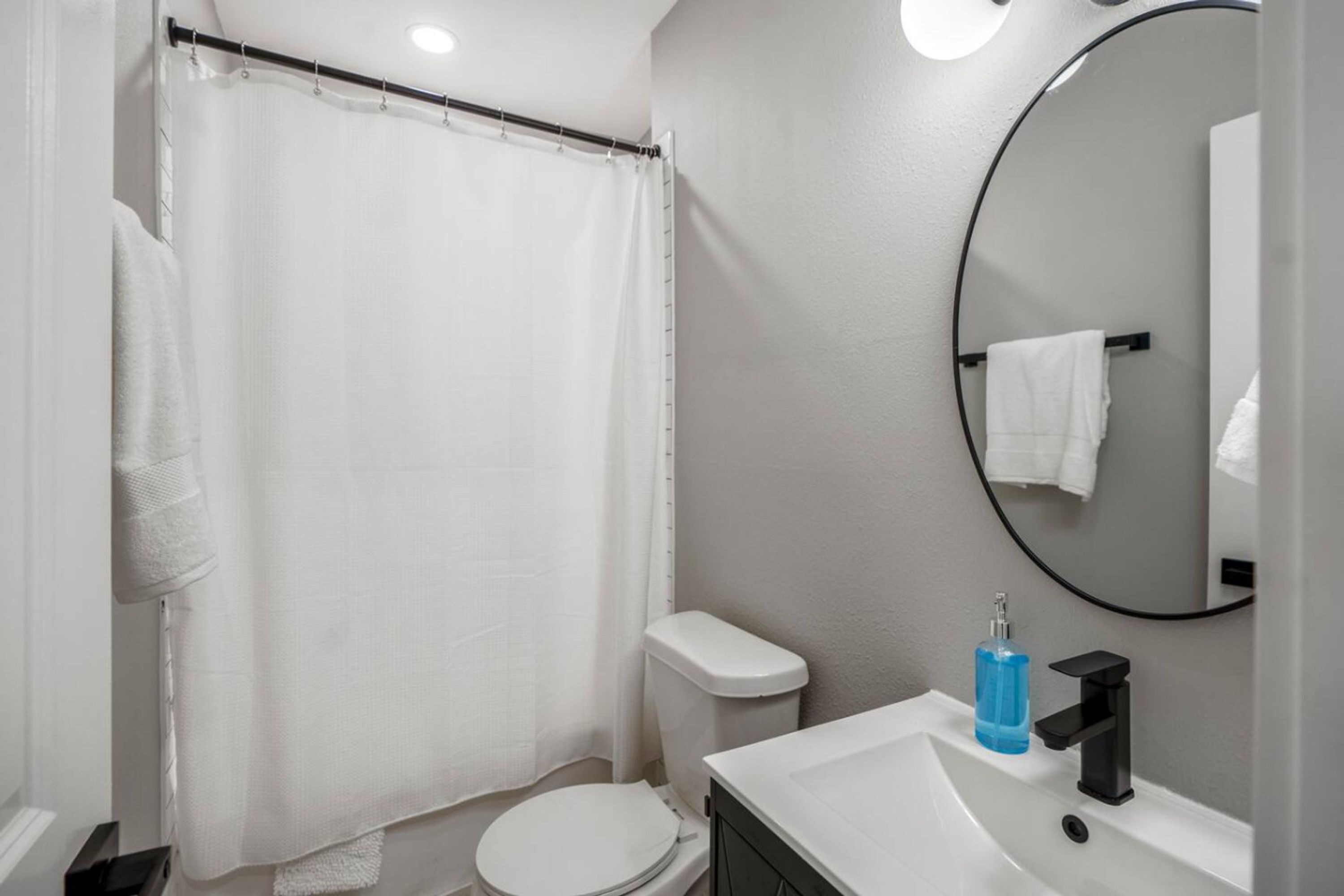 Une salle de bain équipée d’un rideau de douche, de toilettes, d’un lavabo avec un miroir et d’un porte-serviettes.