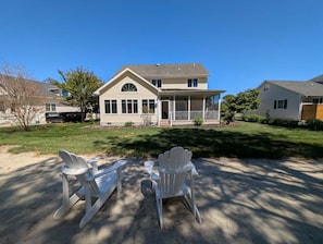 Ein zweistöckiges Haus mit Veranda, Rasen und zwei Adirondack-Stühlen.