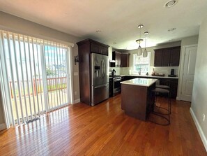 A modern kitchen with a central island, stainless steel appliances, and a sliding glass door leading to a deck.