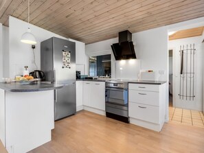 Eine moderne Küche mit weißen Schränken, einem Edelstahl-Kühlschrank, einem eingebauten Ofen und einer schwarzen Dunstabzugshaube.