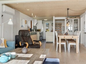 Ein modernes Wohnzimmer mit einer Couch, einem Esstisch mit Stühlen, einer Küchenzeile und einer Holzbalkendecke.
