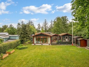 Ein Wohnhaus mit gepflegtem Rasen, mehreren Holzhütten und einem großen Baum im Hintergrund.