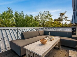 Eine Dachterrasse mit einer Eckcouch, einem Holztisch und Blick auf Bäume.