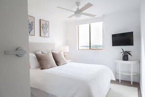 A bedroom with a bed, a ceiling fan, a TV, and a window with a city view. - Bay Breeze Retreat, Glenelg, Absolute Beachfront (Glenelg)