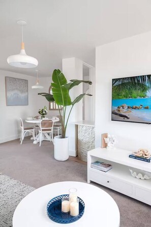 A modern living room with a dining area, a large plant, a TV, and a white console table. - Bay Breeze Retreat, Glenelg, Absolute Beachfront (Glenelg)