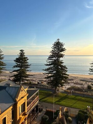 A coastal view with a building, two tall trees, and a beach. - Bay Breeze Retreat, Glenelg, Absolute Beachfront (Glenelg)