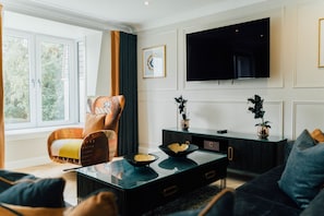 Ein Wohnzimmer mit einer Couch, einem Sessel, einem Couchtisch, einem Fernseher und einem Fenster mit Vorhängen.