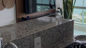 A kitchen with a granite countertop, stainless steel sink, and a flat-screen TV above the counter. - 180-degree sea view (Salvador)