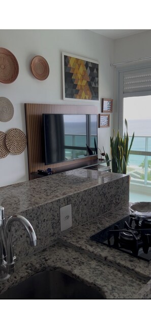 A kitchen with a granite countertop, stainless steel sink, and a flat-screen TV above the counter. - 180-degree sea view (Salvador)
