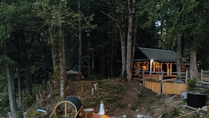 A cabin in a forest with a deck, a circular structure, and a satellite dish.