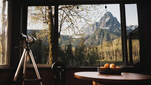A room with a telescope, a round table with oranges, and a mountain view through a window.