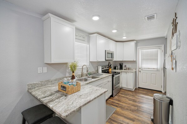 A kitchen with white cabinets, a granite countertop, stainless steel appliances, and a trash can.