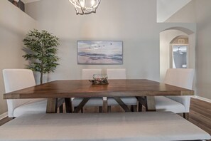 A dining area with a wooden table, cushioned chairs, a potted plant, and a painting of birds over water. - Gorgeous 3BR/2BA Saltwater Pool on Rivard Public Golf Course (Brooksville)