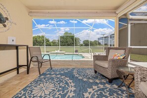 Un patio couvert avec vue sur une piscine, agrémenté de meubles en osier et d’un tapis à motifs.