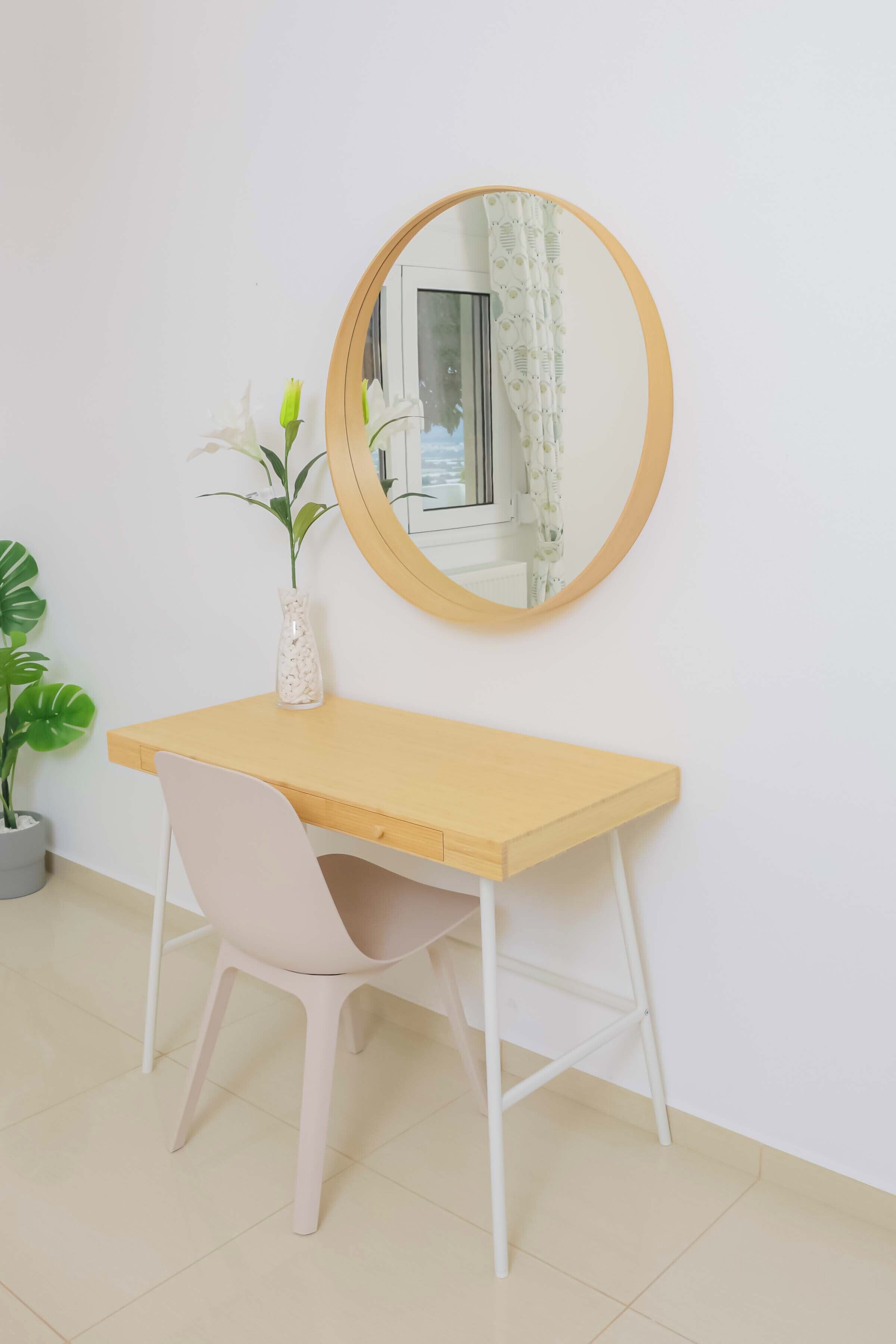 Un bureau en bois, une chaise blanche, un miroir rond et une plante en pot.