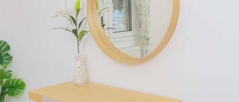 Un bureau en bois, une chaise blanche, un miroir rond et une plante en pot.