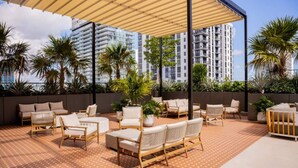 A rooftop terrace with outdoor seating, palm trees, and high-rise buildings in the background. - Corner 2BR with Skyline Views, Rooftop Pool & Spa (Miami)