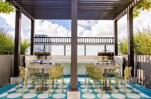 A covered outdoor patio with a grill, seating, and a view of buildings. - Corner 2BR with Skyline Views and Rooftop Pool Minutes to South Beach, Brickell and Wynwood (Miami)