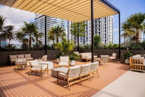 A rooftop patio with outdoor furniture, palm trees, and high-rise buildings in the background. - Accessible Corner 2BR Condo w/ Spa + Rooftop Pool (Miami)