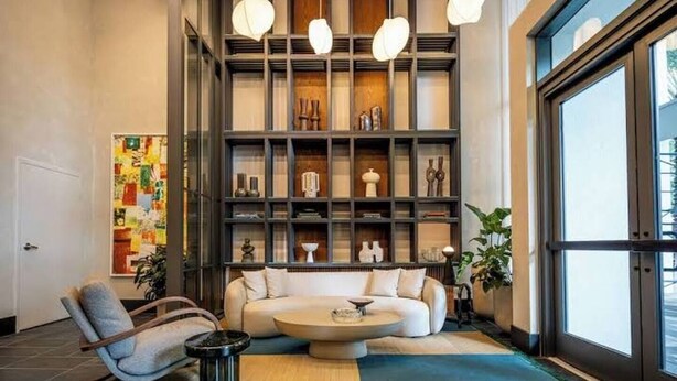 A modern living room with a sofa, a coffee table, a bookshelf, and a large window. - Corner 2BR with Skyline Views, Rooftop Pool & Spa (Miami)