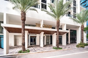 A modern hotel entrance with palm trees, a covered walkway, and a sign reading 'THE CROSBY.' - Accessible Corner 2BR Condo w/ Spa + Rooftop Pool (Miami)