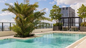 A rooftop pool with clear water, surrounded by palm trees and a view of a high-rise building. - Corner 2BR with Skyline Views, Rooftop Pool & Spa (Miami)