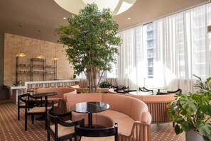 A modern interior with a central seating area, a large tree, and a bar with shelves. - Accessible Corner 2BR Condo w/ Spa + Rooftop Pool (Miami)
