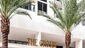A hotel entrance with palm trees, a sign reading 'THE CROSBY,' and a modern building facade. - Corner 2BR with Skyline Views, Rooftop Pool & Spa (Miami)