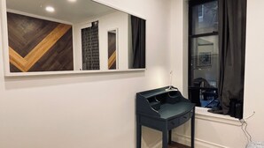 A room with a mirror, a dark-colored desk, a window with curtains, and a wooden floor. - Quiet LES Designer Retro-Chic 1 Bedroom Apt Near Everything (New York)